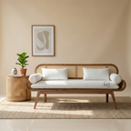 Wooden sofa with white cushions in a room with a plant and framed art on the wall.